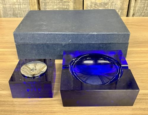 A Pair of Mid-Century Modern Italian Style Cobalt Blue Glass Smoking Accessories: This matched smoking set features a square-profile ashtray and a square table lighter base, both formed from heavy, translucent cobalt blue glass. The design emphasizes solid geometric forms with shar