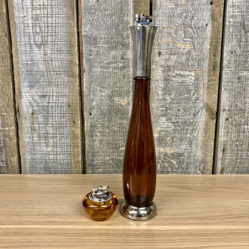 A Pair of Mid-Century Modern Amber Glass Table Lighters Including Viking Glass: This lot features two mid-century modern table lighters composed of amber glass with chrome-finished metal components. The smaller lighter is of a squat, rounded form and retains a partial red and sil