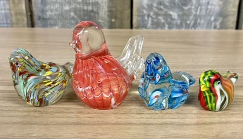 Four Hand-Blown Art Glass Bird Figurines Including Murano and Lefton Examples: A collection of four hand-blown art glass bird figurines in varying sizes and styles. The largest piece features a red and white swirled glass body with a clear glass head and tail; the underside disp