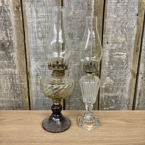 Two Vintage Glass Kerosene Lamps with Optic Swirl and Etched Motifs: This lot features two distinct vintage glass kerosene lamps. The larger lamp consists of a clear pressed glass font with a spiral optic swirl pattern, mounted on a dark amethyst or black glass pedesta