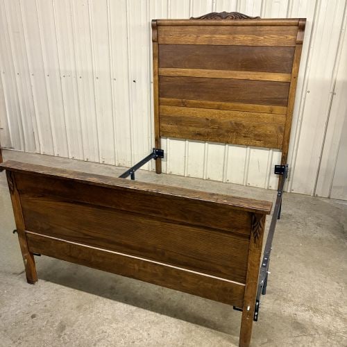Late 19th or Early 20th Century American Empire Style Carved Oak Full Size Bed: An American Empire style bed dating to the late 19th or early 20th century, constructed from oak with a medium-to-dark brown finish. The headboard features a prominent rolled top rail surmounted by a 