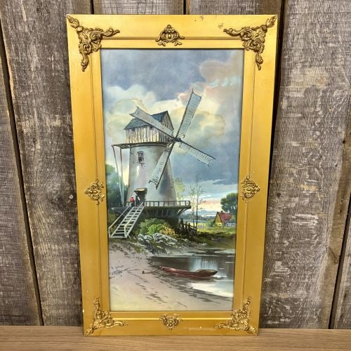 Mid-20th Century Framed Offset Lithograph of a Dutch Windmill Scene: This framed offset lithograph depicts a traditional European windmill situated on a riverbank. The composition features two small figures standing at the elevated entrance of the mill, a red rowboat m