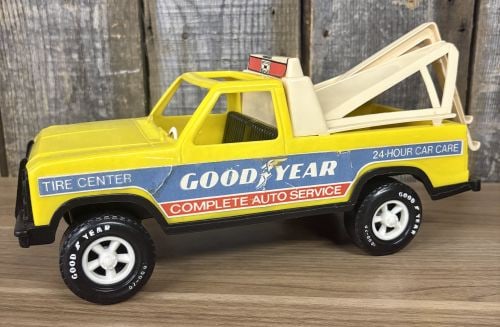 Gay Toys Inc. Goodyear Tire Center Service Tow Truck Item No. 689: This is a vintage molded plastic toy tow truck manufactured by Gay Toys Inc. The vehicle features a bright yellow body with a black front grille, bumper, and interior bench seat. An off-white or cream