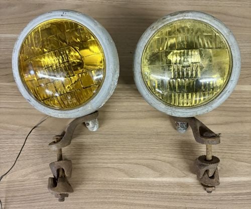 A Pair of Vintage Automotive Fog Lights with Bumper Mount Brackets: This lot consists of a pair of vintage auxiliary automotive fog lamps, typically used as accessories for mid-20th-century vehicles. Each unit features a spherical metal housing and is mounted to a uni