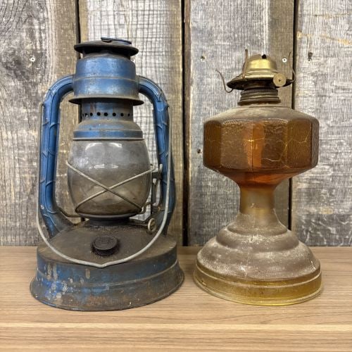 Two Vintage Portable Lamps Including a No. 100 Hurricane Lantern and an Amber Glass Lamp: A pair of vintage portable lighting pieces. The first item is a metal hurricane lantern attributed to Dietz, specifically the Little Wizard No. 100 model. The lantern features a blue-painted frame wit