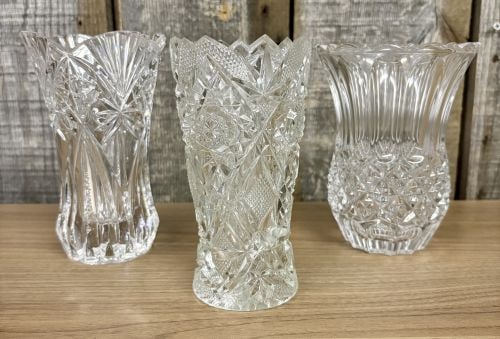 Three clear cut glass and lead crystal decorative vases including one attributed to Cristal d'Arques: This collection consists of three clear glass decorative vases featuring distinct geometric patterns. The first item is a trumpet-shaped vase with a flared, scalloped rim. Its decoration includes larg