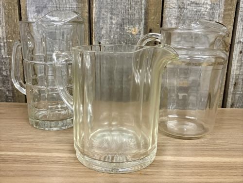A Trio of Vintage American Pressed Glass Water Pitchers: This lot features three vintage pressed glass pitchers, likely produced in the United States during the mid-20th century. The first vessel is a pale yellow citron-toned pitcher characterized by wide v