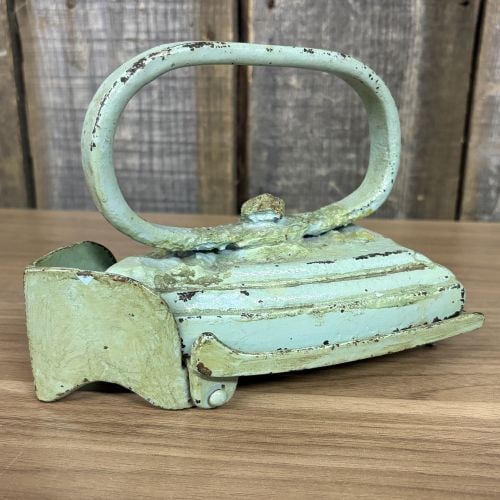 A Pair of Antique Cast Iron Miniature Sad Iron and Matching Footed Trivet: This set features a late 19th to early 20th-century miniature cast iron sad iron and a coordinating footed trivet. The iron is a single-piece casting with a pointed nose, a flat base, and a fixed loop