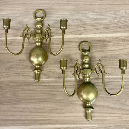 A Pair of Vintage Colonial Revival Style Cast Brass Double Arm Wall Sconces: This pair of vintage wall-mounted candle sconces is constructed from cast brass in a traditional Colonial Revival style. Each piece features a central vertical column characterized by turned elements 