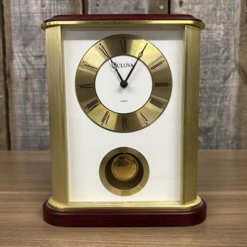 Bulova Gold-Tone and Wood-Finished Quartz Mantel Clock with Pendulum: This Bulova quartz mantel clock is constructed with a rectangular gold-tone metal frame featuring fluted columnar supports and a dark wood-finished top and base. The dial assembly consists of a gold-t