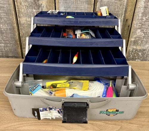 Flambeau Outdoors Three-Tray Plastic Fishing Tackle Box with Assorted Lures and Accessories: A Flambeau Outdoors three-tray fishing tackle box featuring a navy blue lid and light gray base. The interior contains three navy blue cantilevered trays with molded-in ruler markings and embossed dia