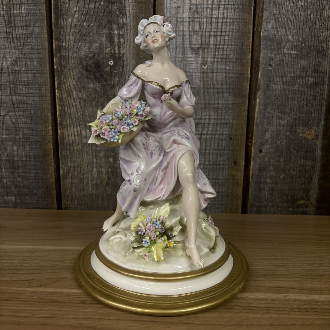 Capodimonte Cesare Villari Porcelain Figurine of a Seated Lady with Flower Basket: A hand-painted polychrome glazed porcelain figurine designed by Cesare Villari for Capodimonte. The piece depicts a seated lady in 18th-century Rococo attire, featuring a lavender-pink dress with flor