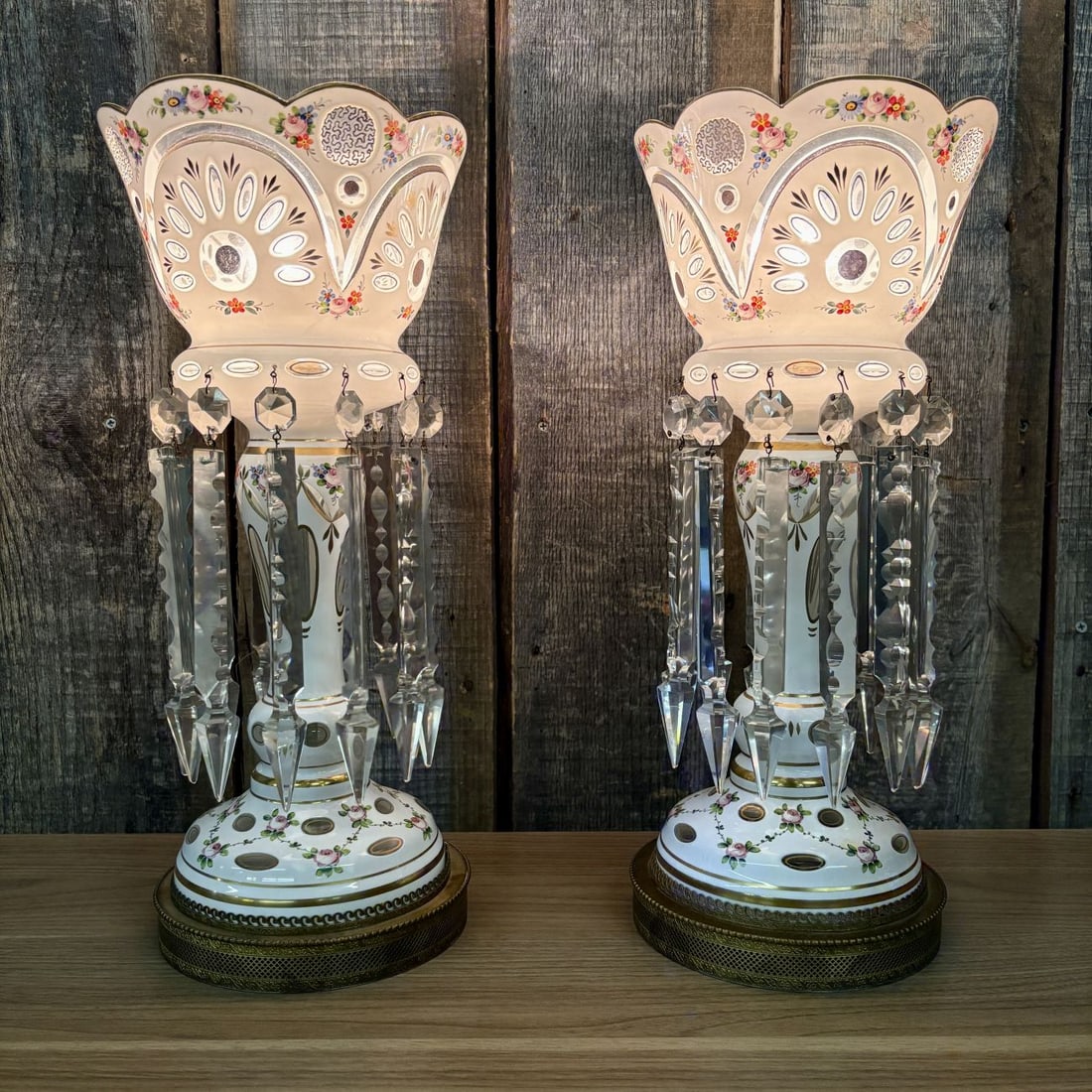 A Pair of Bohemian White Cased Glass Mantle Luster Lamps: This pair of electrified mantle lamps is fashioned from Bohemian cased glass lusters. Each lamp features white glass overlay cut to clear glass, revealing a series of decorative portals in oval and te