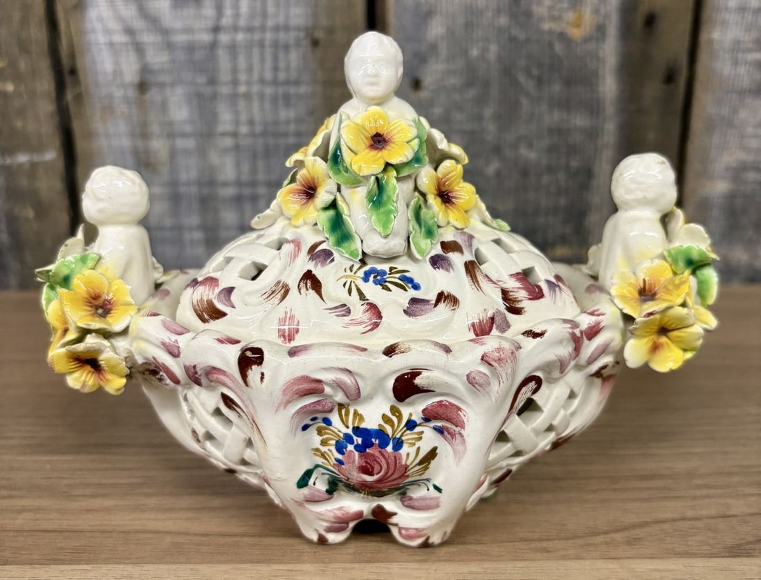Italian Reticulated Majolica Lidded Bowl with Putti and Applied Flowers: This lot features a vintage Italian majolica lidded bowl crafted with a footed base and intricate pierced lattice work. The piece is decorated with hand-painted floral motifs including a central rose 