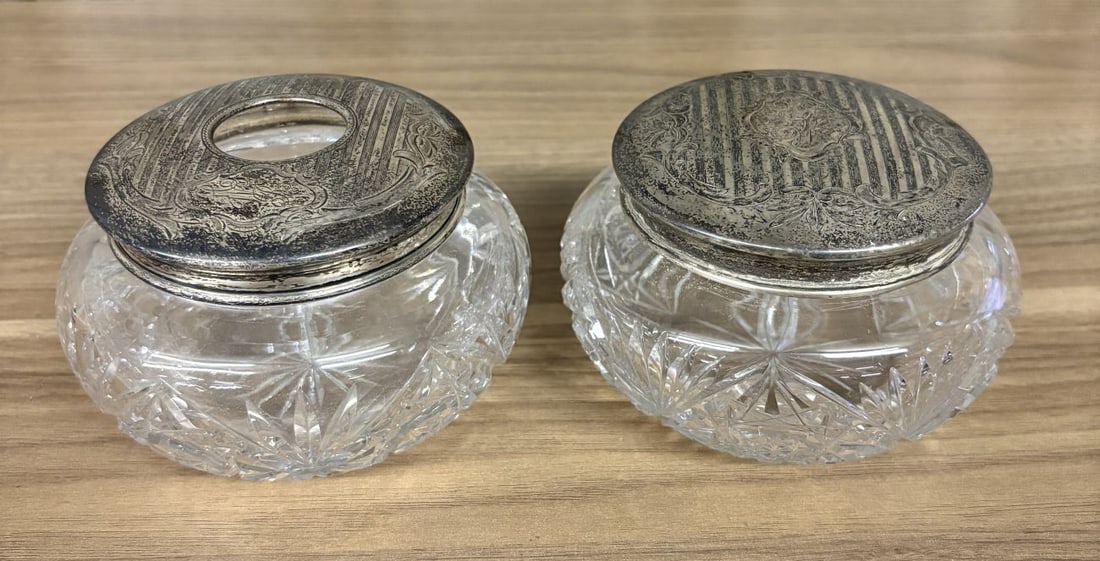 A Pair of Antique Sterling Silver and Cut Glass Vanity Jars: This matching pair of vanity jars includes one hair receiver and one solid lid dresser jar, likely dating to the late nineteenth or early twentieth century. The jars are made of heavy cut glass in the