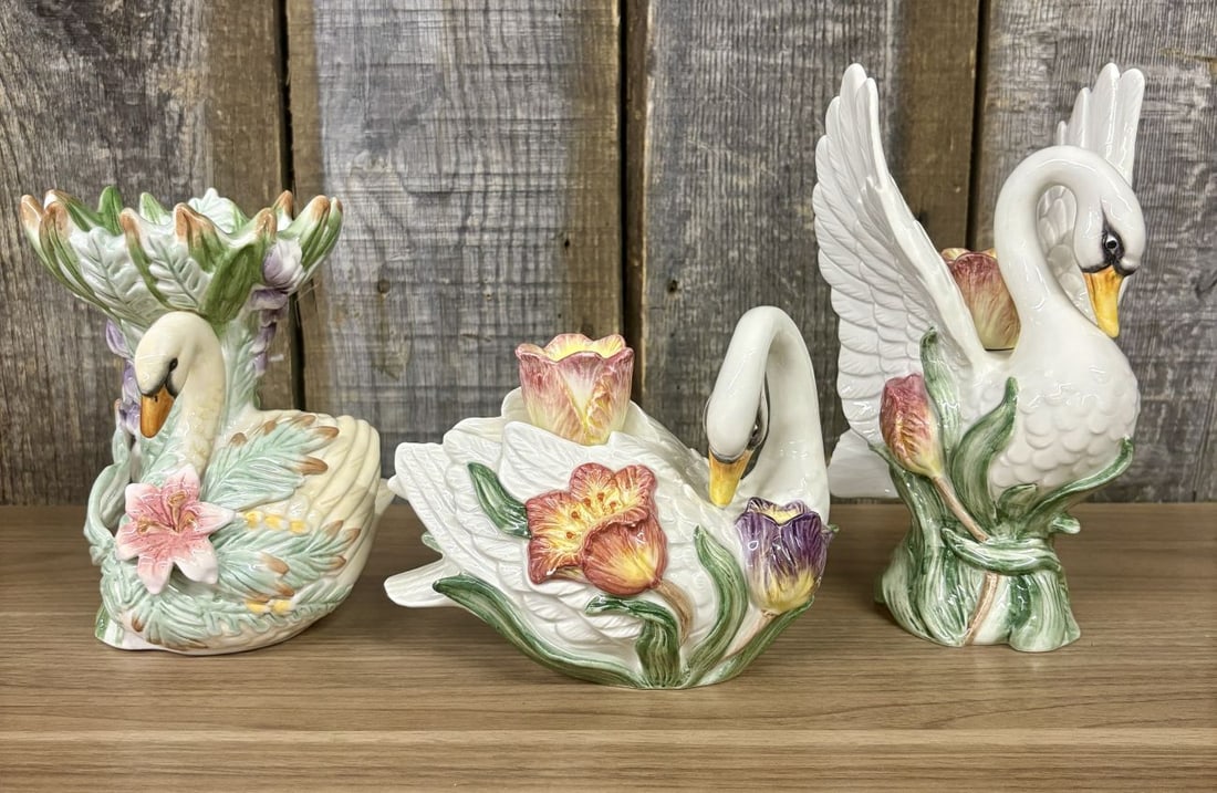 A Trio of Fitz and Floyd Tulip Swan Pattern Porcelain Decorative Items: This set of glazed porcelain china from Fitz and Floyd features the Tulip Swan pattern. The collection includes one small vase or planter and two distinct candle holders. Each piece is decorated with 