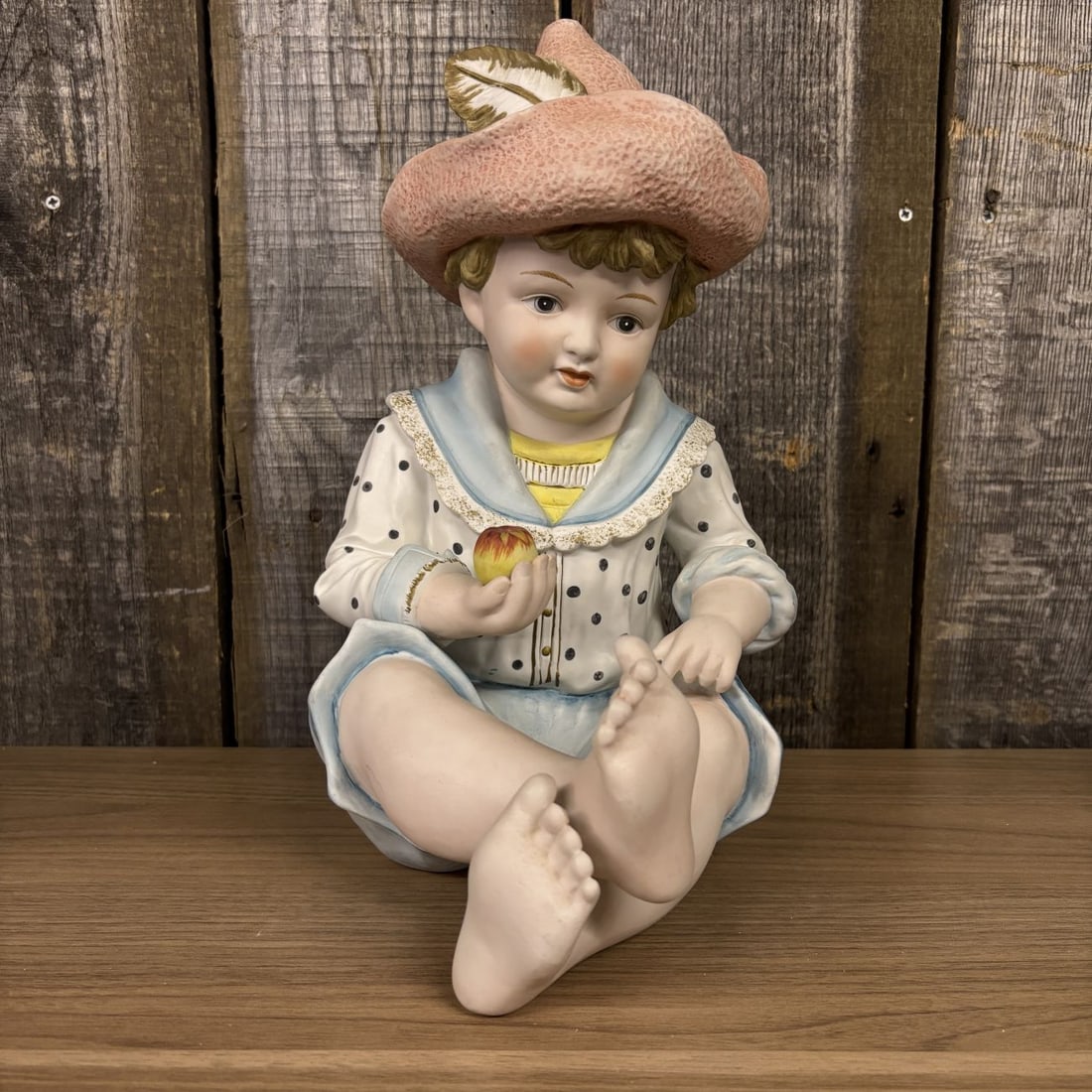 Andrea by Sadek Bisque Porcelain Piano Baby Boy Figurine Model 6161: A hand-painted bisque porcelain piano baby figurine produced by Andrea by Sadek. The figure depicts a seated young boy with light brown hair and rosy cheeks holding a small red and yellow apple in his