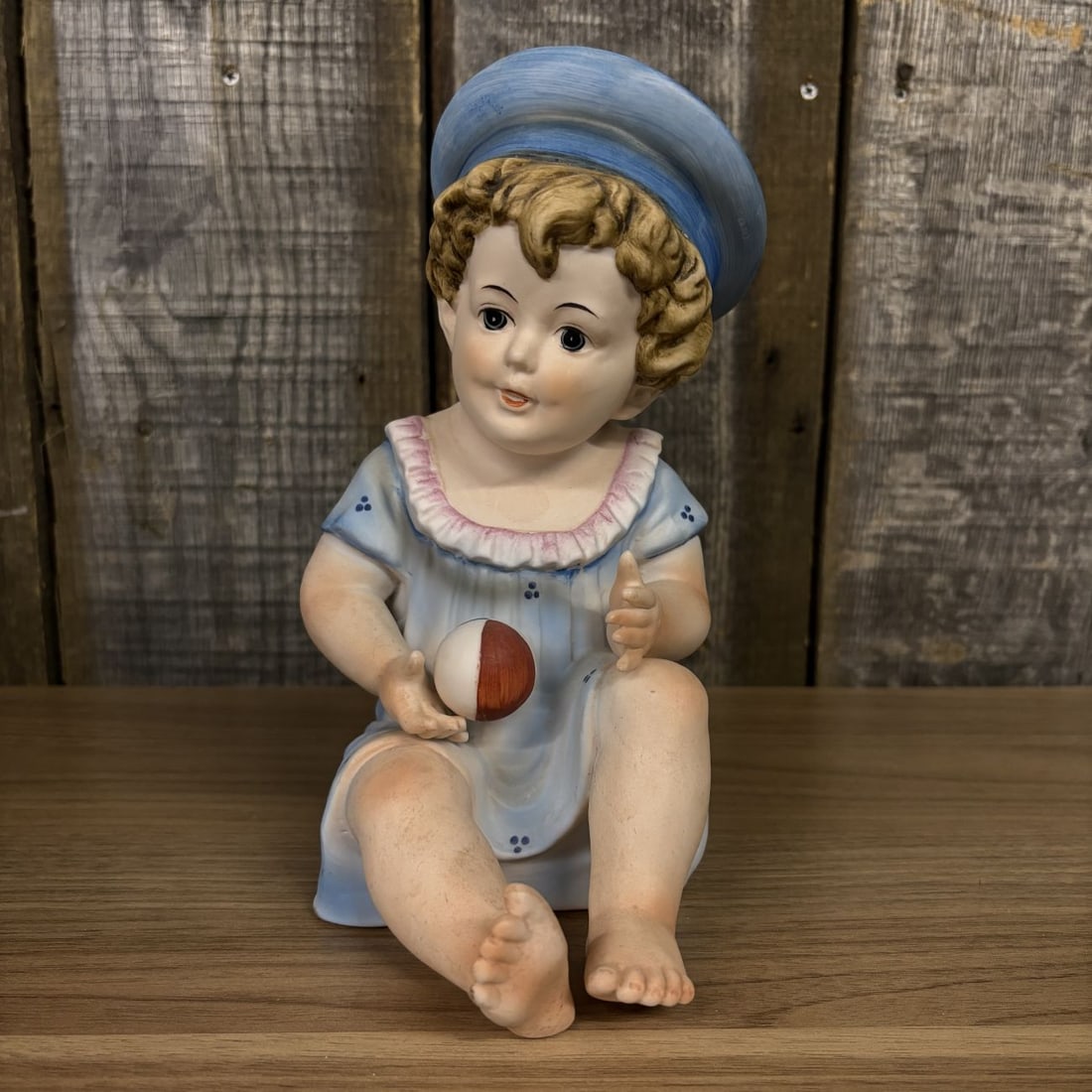 Large Antique German Bisque Porcelain Piano Baby Figurine: A large antique German bisque porcelain piano baby figurine depicting a seated young child. The figure is rendered with a matte finish and hand-painted details. The child is dressed in a light blue ga