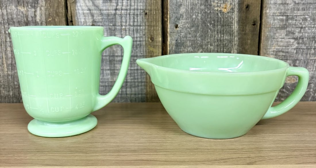 Two Pieces of Fire-King Jade-ite Glassware Including 1-Quart Measuring Pitcher and Batter Bowl: This lot consists of two pieces of vintage Jade-ite glassware manufactured by Fire-King. The first item is a footed 1-quart measuring pitcher featuring a D-shaped handle and an integrated pouring spou