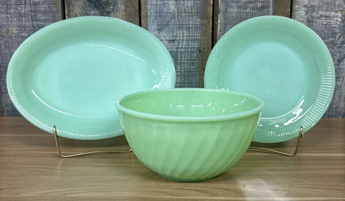A Trio of Fire-King Jadeite Glass Tableware Including Jane Ray and Swirl Patterns: This set of three opaque green glass items, commonly known as jadeite, was produced by Anchor Hocking for the Fire-King line. The grouping consists of one oval platter and one round dinner plate in th