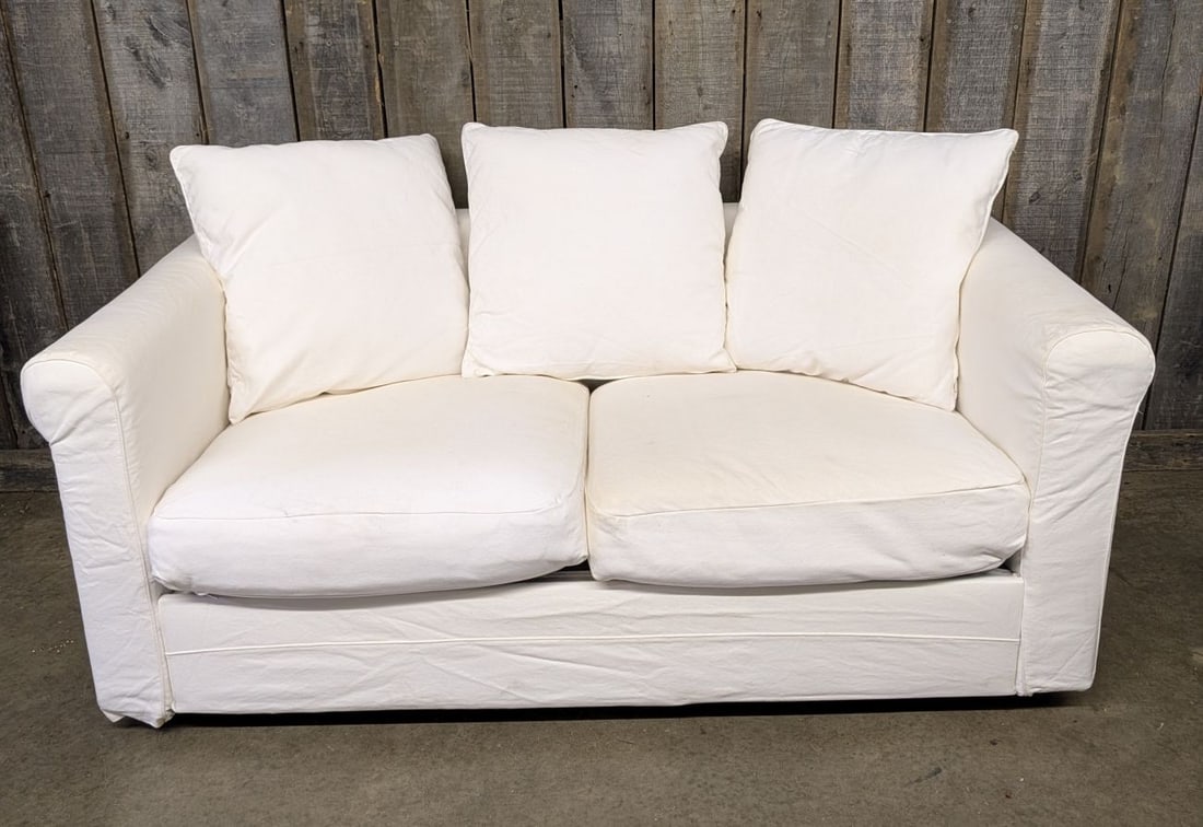 Contemporary Slipcovered Two Seat Sofa with Rolled Arms: A contemporary casual two seat sofa featuring a white canvas or heavy cotton slipcover. The design includes rolled arms, two loose seat cushions, and three loose square back pillows. The furniture fra