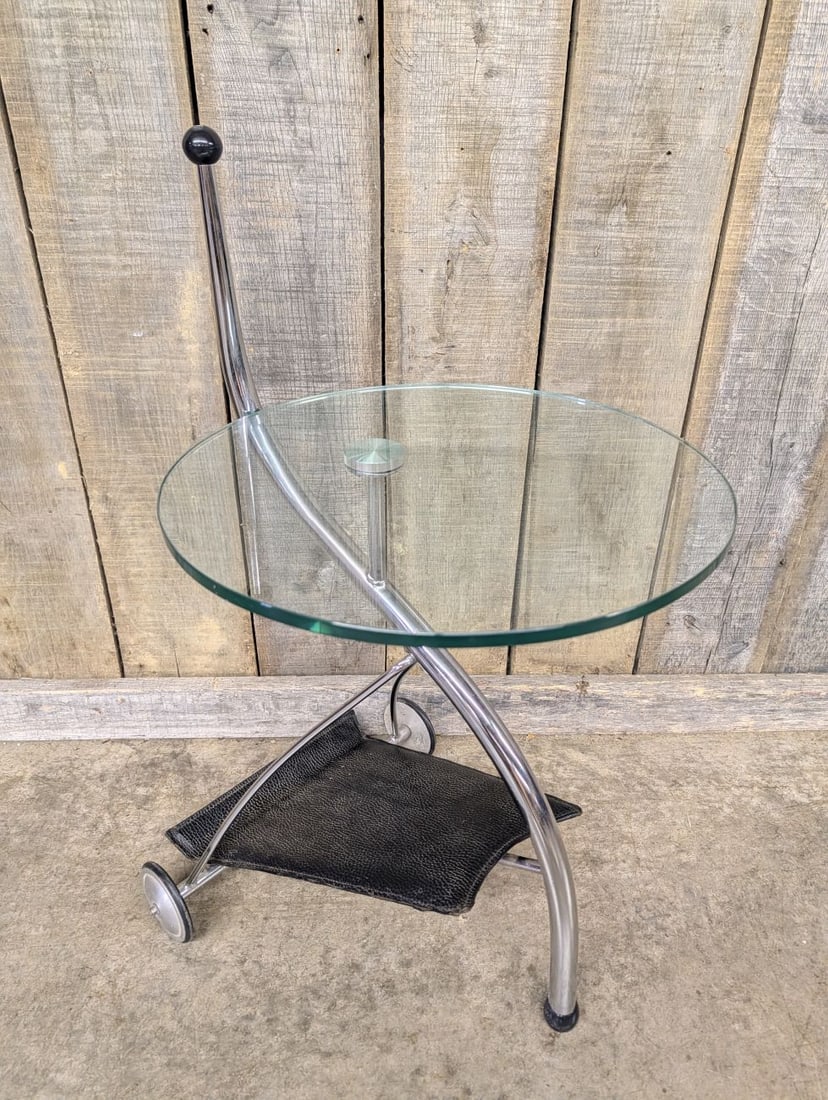 Modern Chrome and Glass Mobile Side Table with Textured Sling Shelf: This mobile side table or bar cart features a minimalist modern design. The frame is constructed from curved, chrome-plated tubular steel in a tripod configuration. The circular top is made of clear t