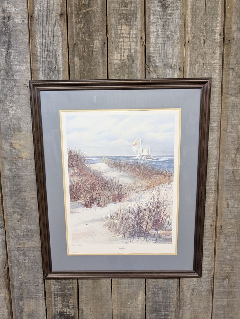 Jacqueline Penney, Heading Out, Large Framed Collograph Print, 1984: A large-scale photomechanical print titled Heading Out by artist Jacqueline Penney. The scene depicts a coastal landscape featuring tall beach grass on sand dunes in the foreground and a large sailboa