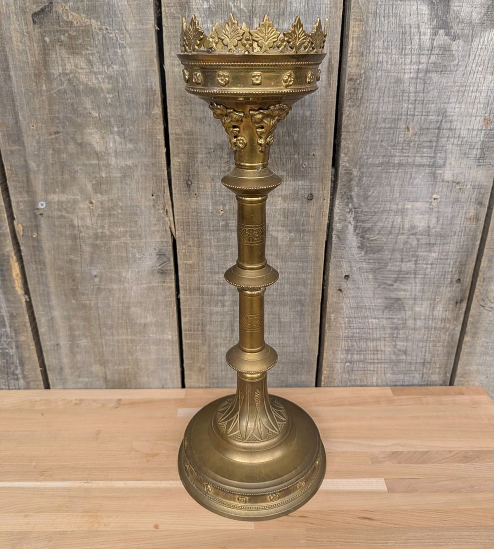Large Gothic Revival Brass Ecclesiastical Pricket Candlestick: A large ecclesiastical-style pricket candlestick constructed of cast brass. The piece features a prominent crown-form top with a crenelated border of stylized foliate leaves above a decorative frieze 