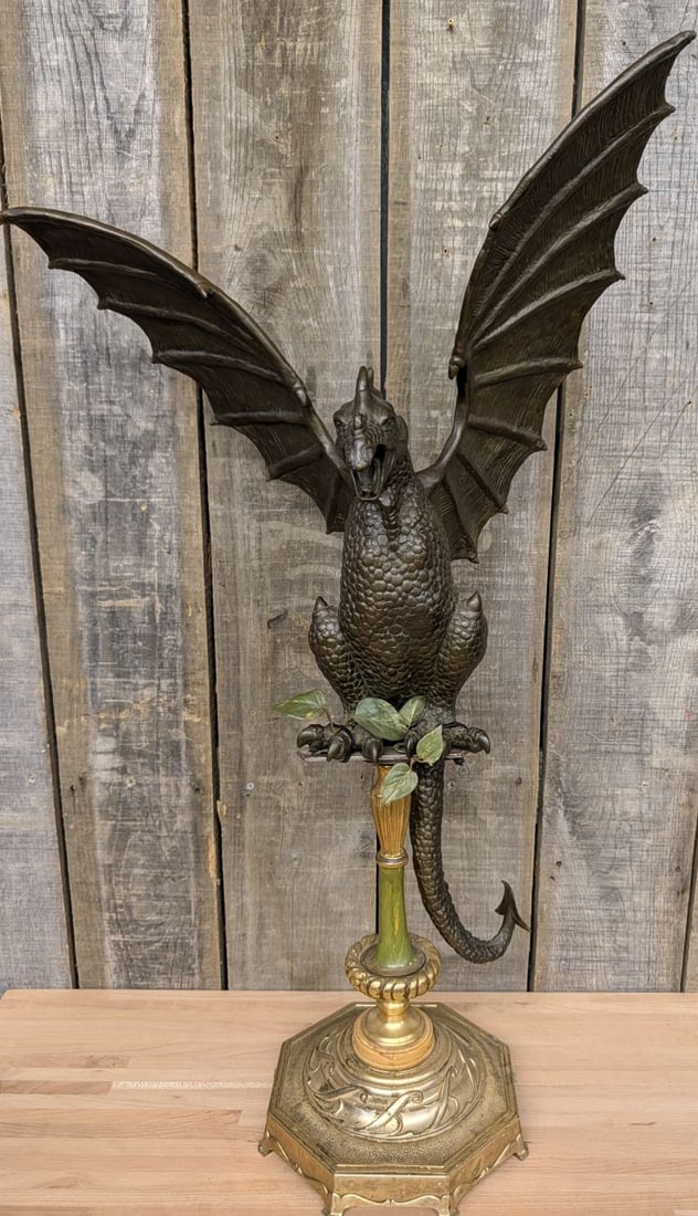 Large Cast Bronze Winged Dragon Sculpture on Decorative Pedestal Stand: This large-scale cast metal sculpture, likely bronze, depicts a winged dragon in an upright perched position. The dragon features a dark brown patina and an intricately textured surface representing s