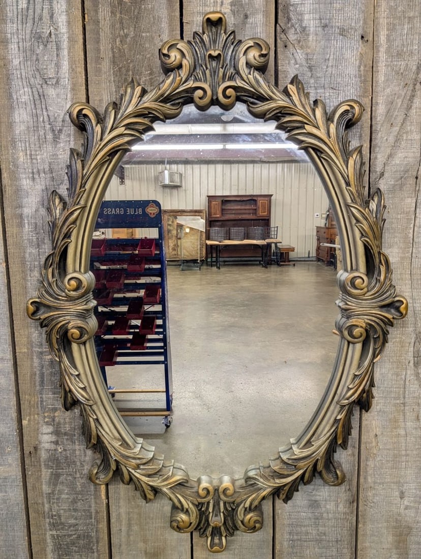 Large Ornate Rococo Revival Gilded Composite Oval Wall Mirror Dated 1972: This large scale oval wall mirror is designed in the Rococo Revival style, featuring a frame constructed from molded synthetic composite material with a hollow-back design. The frame is decorated with