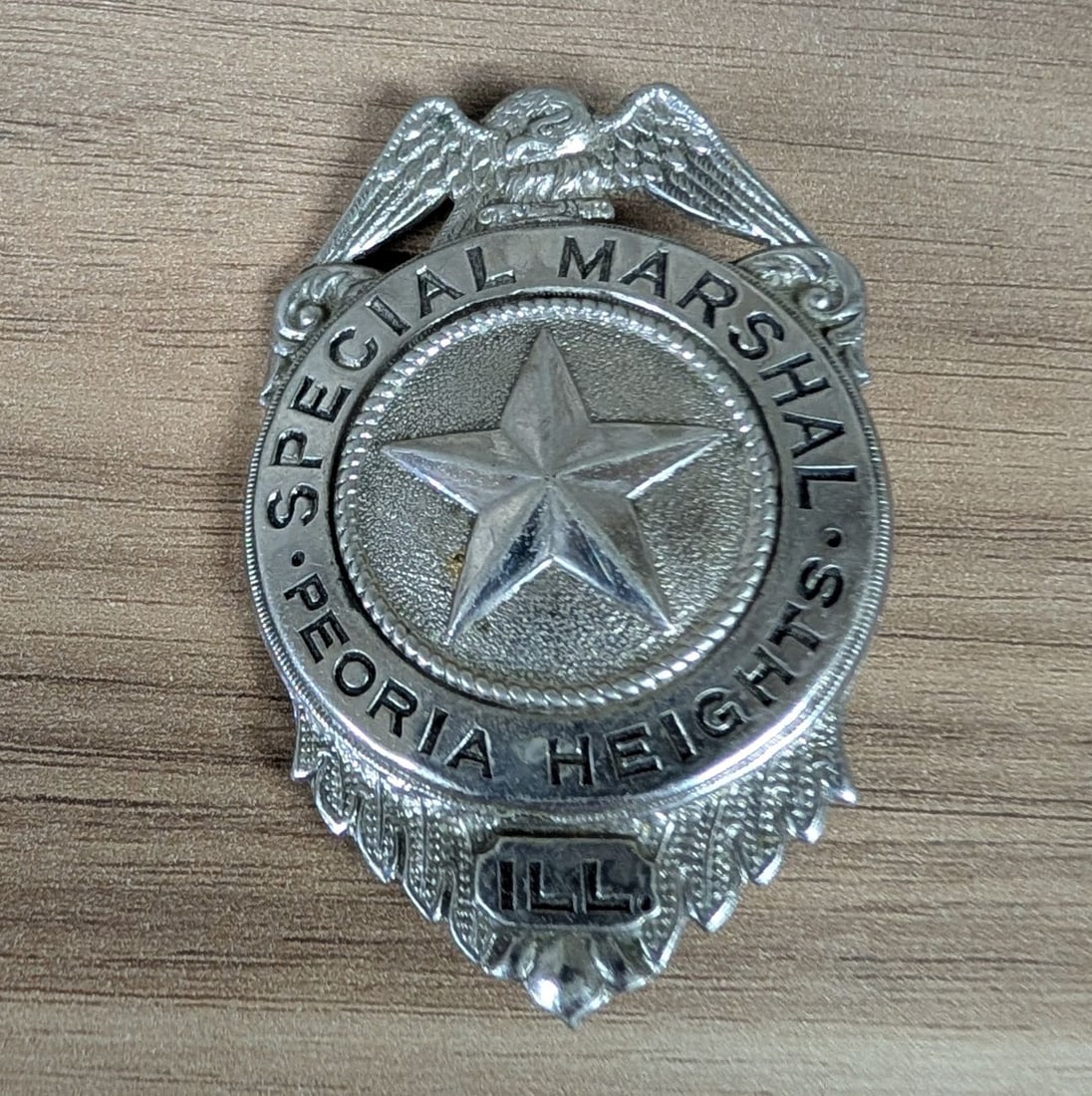Vintage Peoria Heights Illinois Special Marshal Silver Toned Shield Badge: A vintage law enforcement badge from Peoria Heights, Illinois. The badge is constructed in a traditional shield format, topped with a spread-winged eagle clutching a bundle of arrows and an olive bran