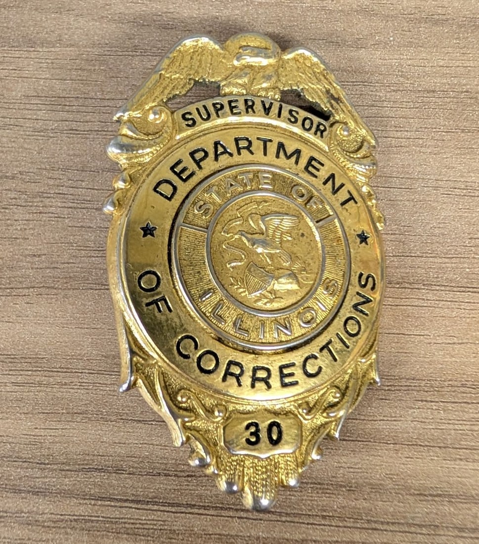 Obsolete Illinois Department of Corrections Supervisor Badge Number 30: This is an obsolete law enforcement breast badge for the State of Illinois Department of Corrections. The badge is constructed from die-struck gold-toned metal with silver-toned highlights. It feature