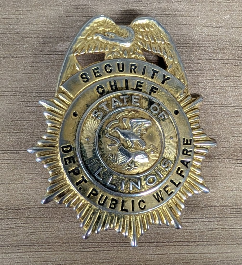 Obsolete State of Illinois Department of Public Welfare Security Chief Badge: A mid-20th-century obsolete security badge for the rank of Security Chief within the Illinois Department of Public Welfare. The badge is constructed in a traditional eagle-top sunburst design. The top