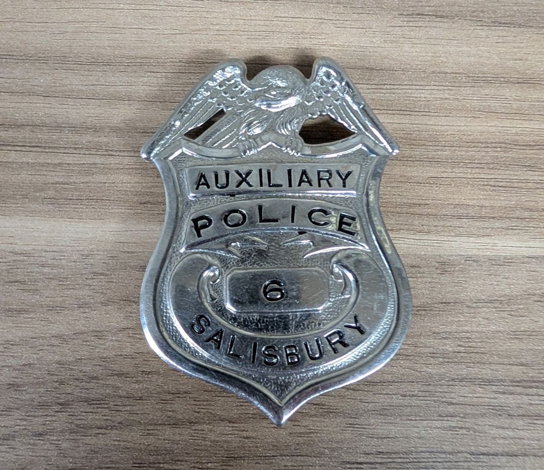 Obsolete Salisbury Maryland Auxiliary Police Badge Number 6 by George W. Smith: This is an obsolete silver-toned metal auxiliary police badge manufactured by the George W. Smith company of Baltimore, Maryland. The shield-style badge is topped with a spread-wing eagle crest. The f