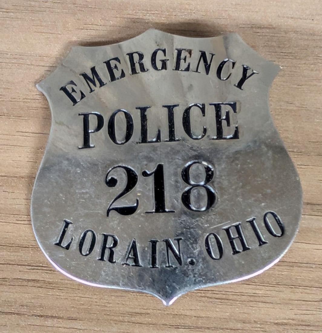 Obsolete Lorain, Ohio Emergency Police Badge Number 218: An obsolete shield-form Emergency Police badge from Lorain, Ohio, dating to the mid-20th century. The badge is constructed from a single piece of stamped metal with a polished silver-toned finish. The