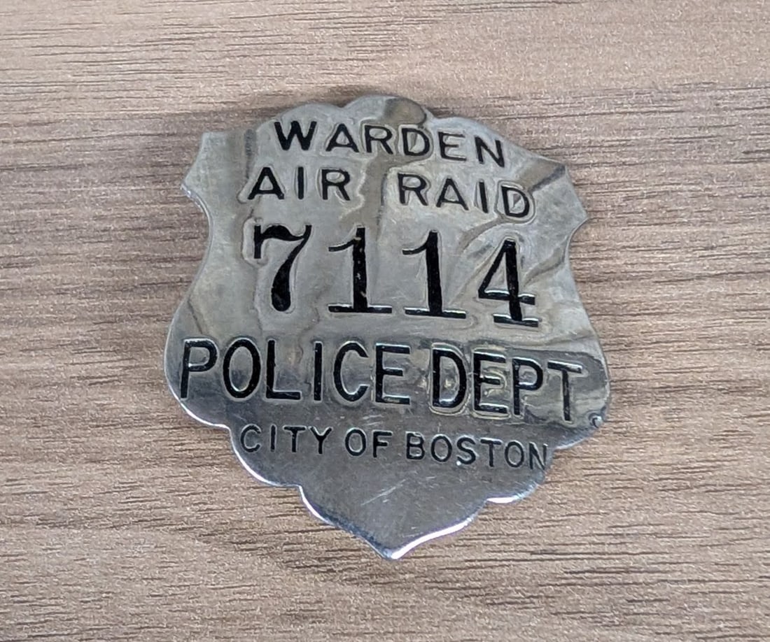 WWII City of Boston Police Department Air Raid Warden Badge Number 7114: Original World War II-era civil defense badge issued by the City of Boston Police Department to a volunteer Air Raid Warden. The badge is a shield-style design with scalloped top and bottom edges, man