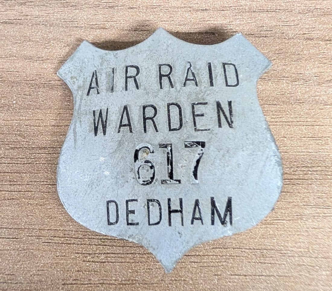 WWII US Civilian Defense Air Raid Warden Identification Badge Dedham Massachusetts: This is a shield-shaped identification badge issued to a civilian Air Raid Warden during World War II. The badge is constructed from a non-precious white metal or zinc alloy, a material choice typical