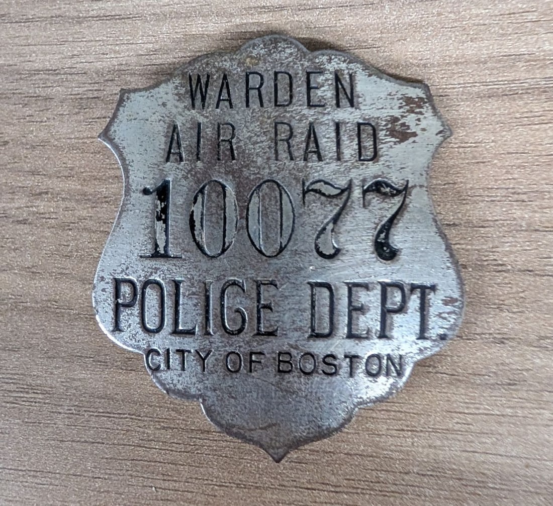 WWII City of Boston Police Department Air Raid Warden Badge No. 10077: This is a World War II-era civilian defense badge issued by the Boston Police Department for an Air Raid Warden. The badge is constructed of stamped metal with a silver-tone finish and features black 