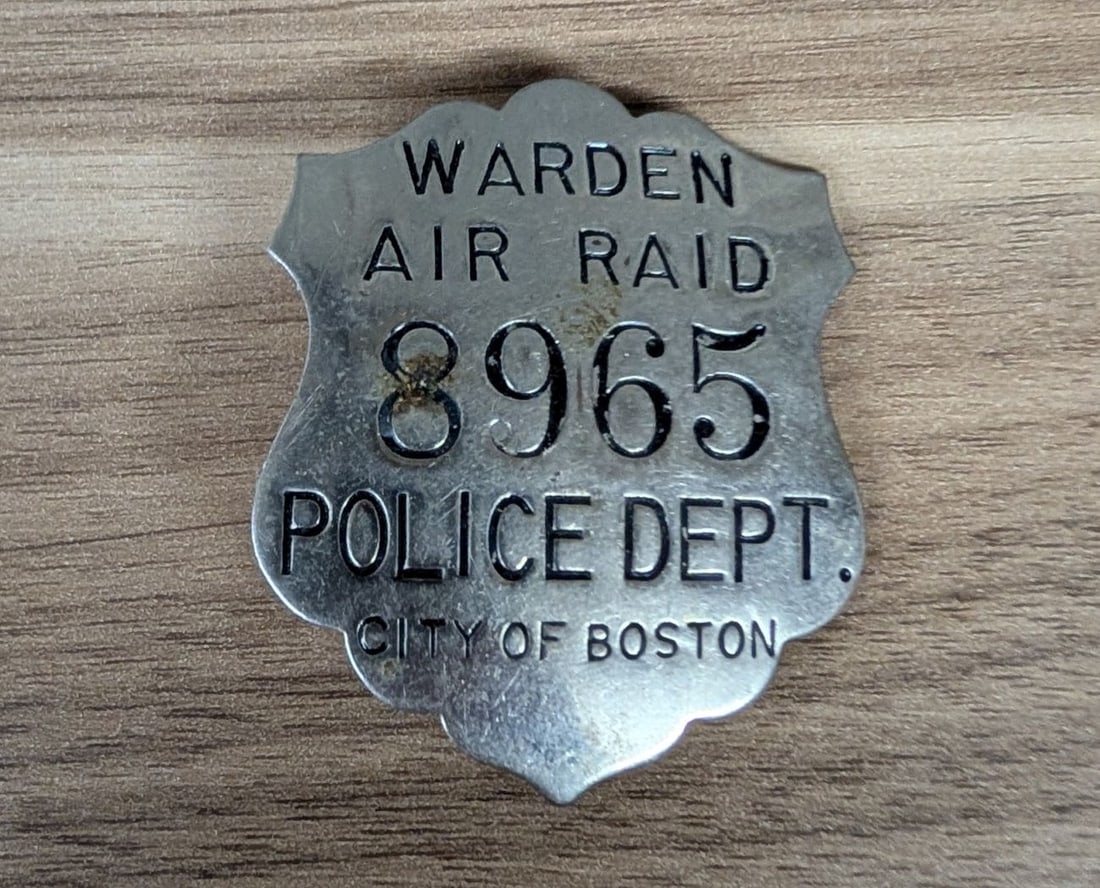 WWII City of Boston Police Department Air Raid Warden Badge, Number 8965: A World War II-era Civil Defense badge issued to an Air Raid Warden by the City of Boston Police Department. This die-stamped metal badge is shield-shaped with scalloped edges at the top and bottom. I