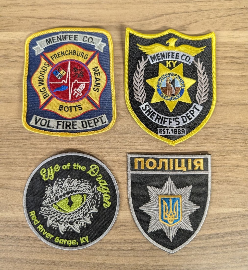 A Lot of Four Assorted Contemporary Embroidered Emergency Service and Commemorative Patches: A collection of four contemporary embroidered patches including emergency service insignia from Menifee County, Kentucky, and the National Police of Ukraine, alongside a regional souvenir patch. The f