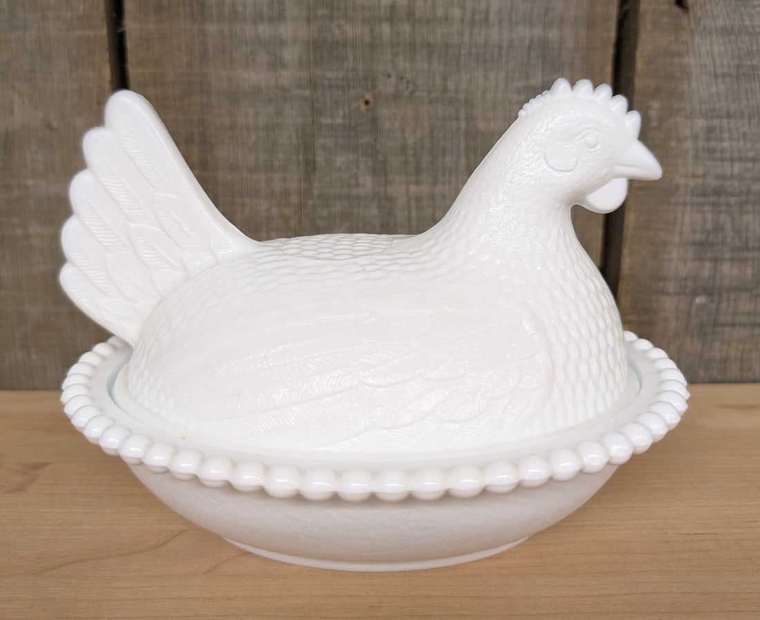 Indiana Glass White Milk Glass Hen on Nest Covered Dish: An Indiana Glass Company white milk glass covered dish in the form of a hen on a nesting base. The two-piece set is crafted from opaque white glass. The lid is molded in the shape of a nesting hen, fe