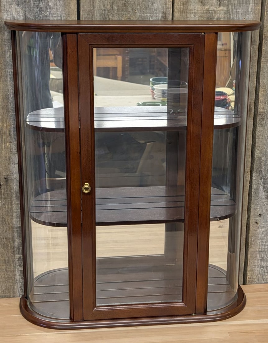 The Bombay Company Curved Glass Wood Wall Curio Cabinet: This wall-mounted curio display cabinet is manufactured by The Bombay Company. It features a bow-front design constructed of wood with a dark mahogany-toned finish. The cabinet is designed with two cu