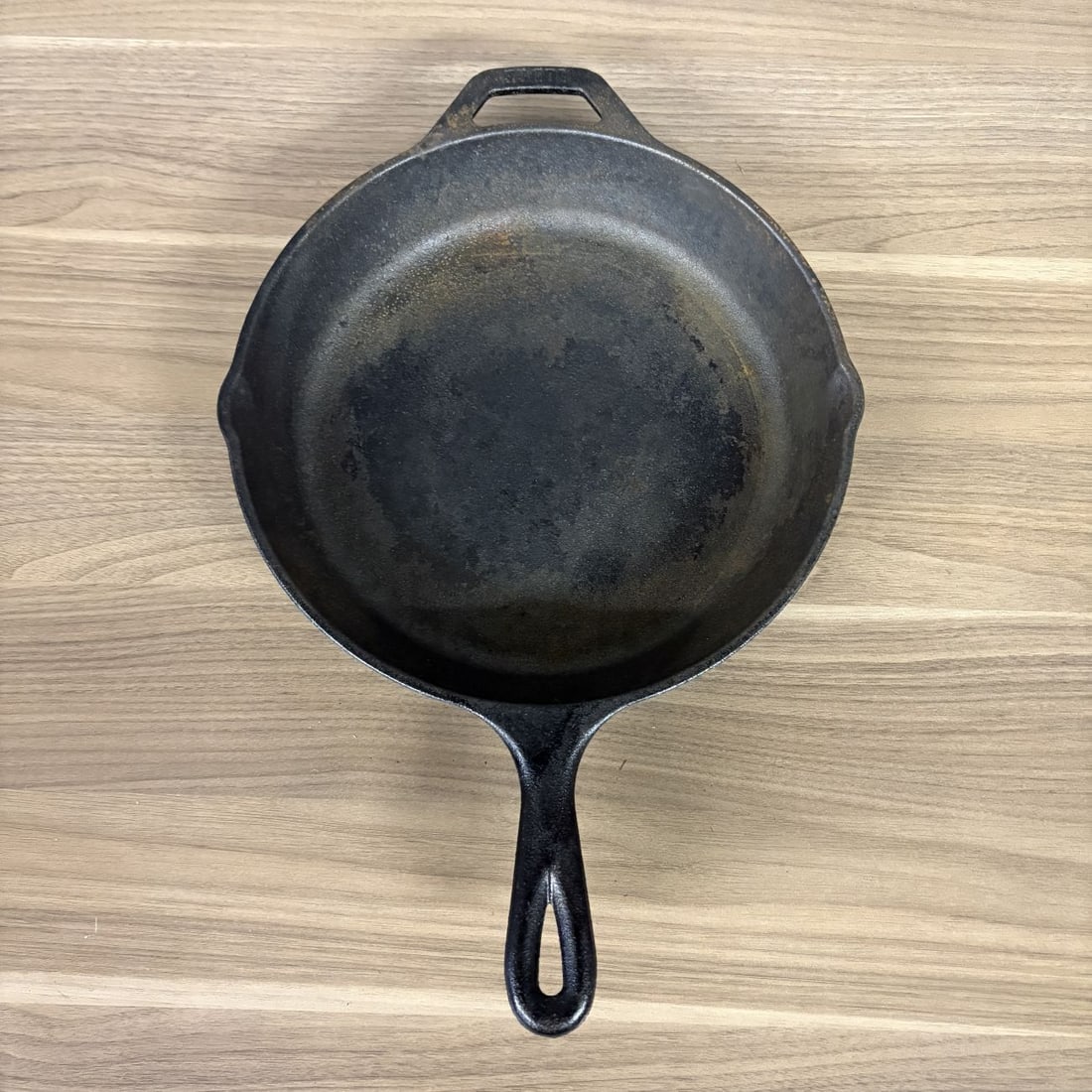 Lodge Cast Iron No. 12 Skillet with Helper Handle: A large cast iron skillet manufactured by Lodge in the United States. This #12 model features a circular design with two integrated pour spouts and a helper handle located opposite the primary handle.
