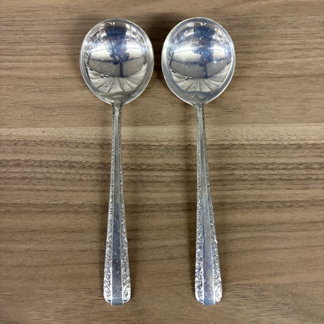 A Pair of Towle Candlelight Pattern Sterling Silver Cream Soup Spoons: A pair of sterling silver cream soup spoons in the Candlelight pattern by Towle Silversmiths. This pattern features a decorative border of flowers and scrolls along the edges of the handle framing a p