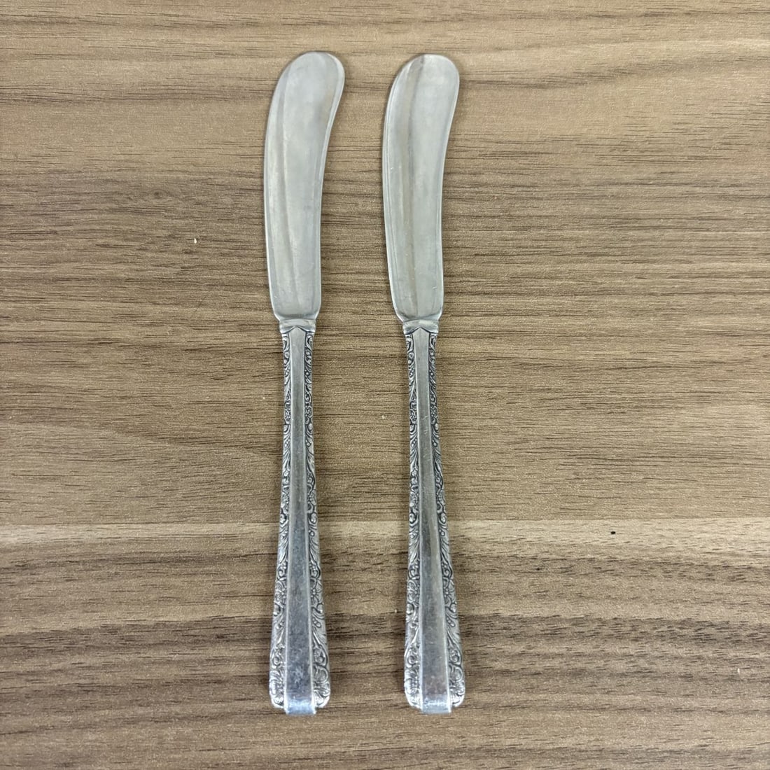 A Pair of Towle Candlelight Pattern Sterling Silver Flat Handle Butter Spreaders: A pair of sterling silver flat handle butter spreaders in the Candlelight pattern by Towle. The pattern is characterized by a floral and scroll motif along the edges of the handle with a plain central