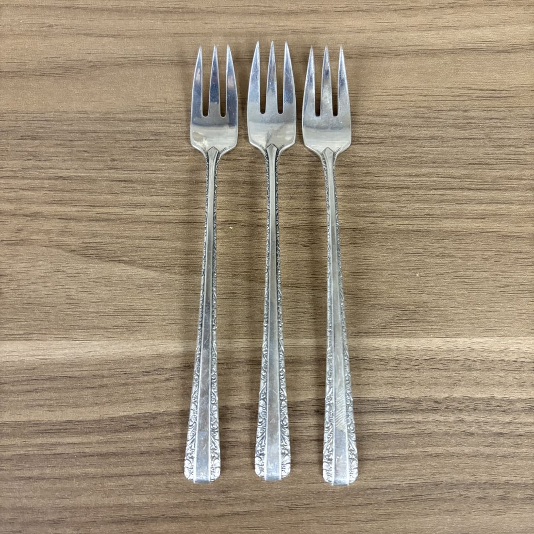 A Trio of Towle Sterling Silver Cocktail Forks in the Candlelight Pattern: A trio of sterling silver cocktail or seafood forks in the Candlelight pattern by Towle Silversmiths. Each fork features three sharp tines and a tapered handle decorated with foliate and scrollwork bo