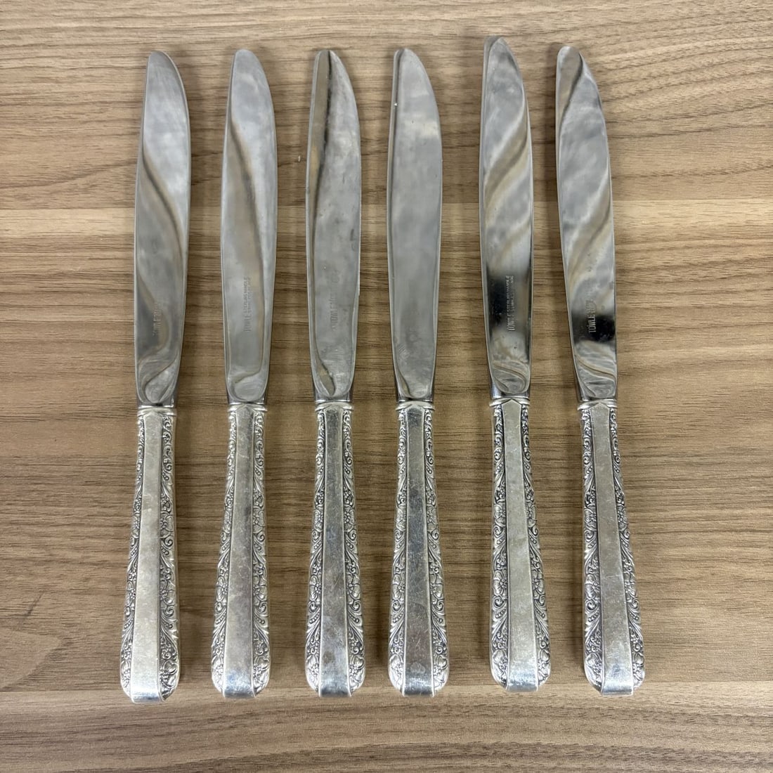 A Set of Six Towle Sterling Silver Handled Dinner Knives in the Rambler Rose Pattern: This set of six dinner knives was manufactured by Towle Silversmiths of Newburyport, Massachusetts. The knives are designed in the Rambler Rose pattern, which was first introduced in 1937. The handles