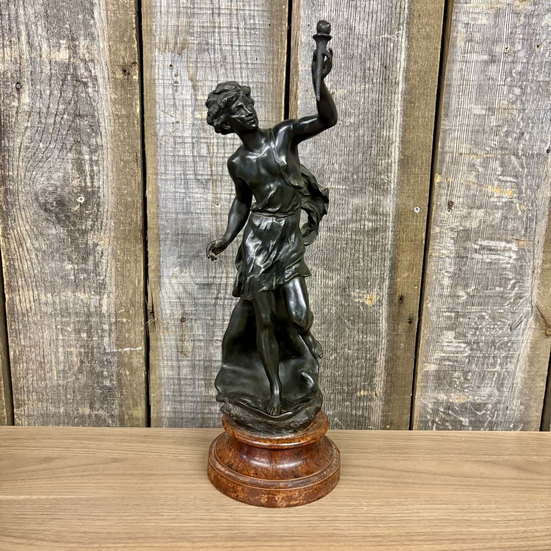Fabrication Francaise Paris Neoclassical Spelter Sculpture of a Youth with Torch: This patinated metal sculpture, cast in spelter, depicts a neoclassical youth in a dynamic mid-stride pose, holding a torch aloft in his right hand. The figure is rendered with fluid movement, clad in