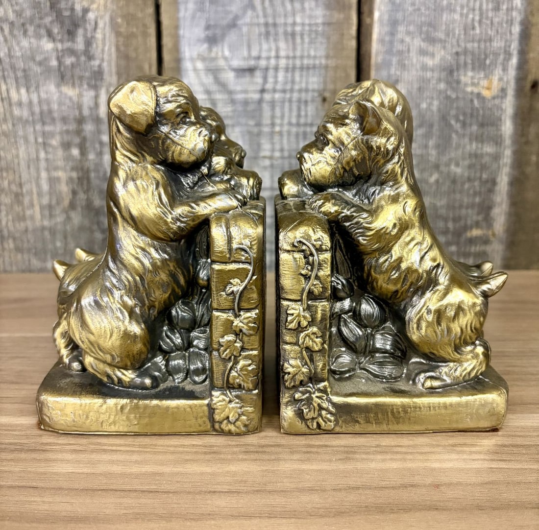A Pair of Vintage Cast Metal Terrier and Puppy Bookends with Gold Toned Finish: A pair of vintage bookends featuring a canine theme, constructed from cast white metal with a gold-toned finish. The design depicts a larger terrier dog, possibly a West Highland White or Cairn Terrie
