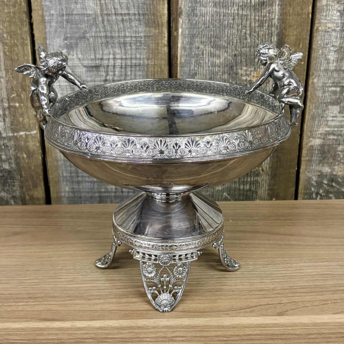 James W. Tufts Victorian Silver Plated Figural Cherub Centerpiece Bowl: A Victorian silver plated centerpiece bowl manufactured by James W. Tufts of Boston. The object is a figural compote featuring a wide, shallow bowl with a rim decorated with a cast band of anthemion a
